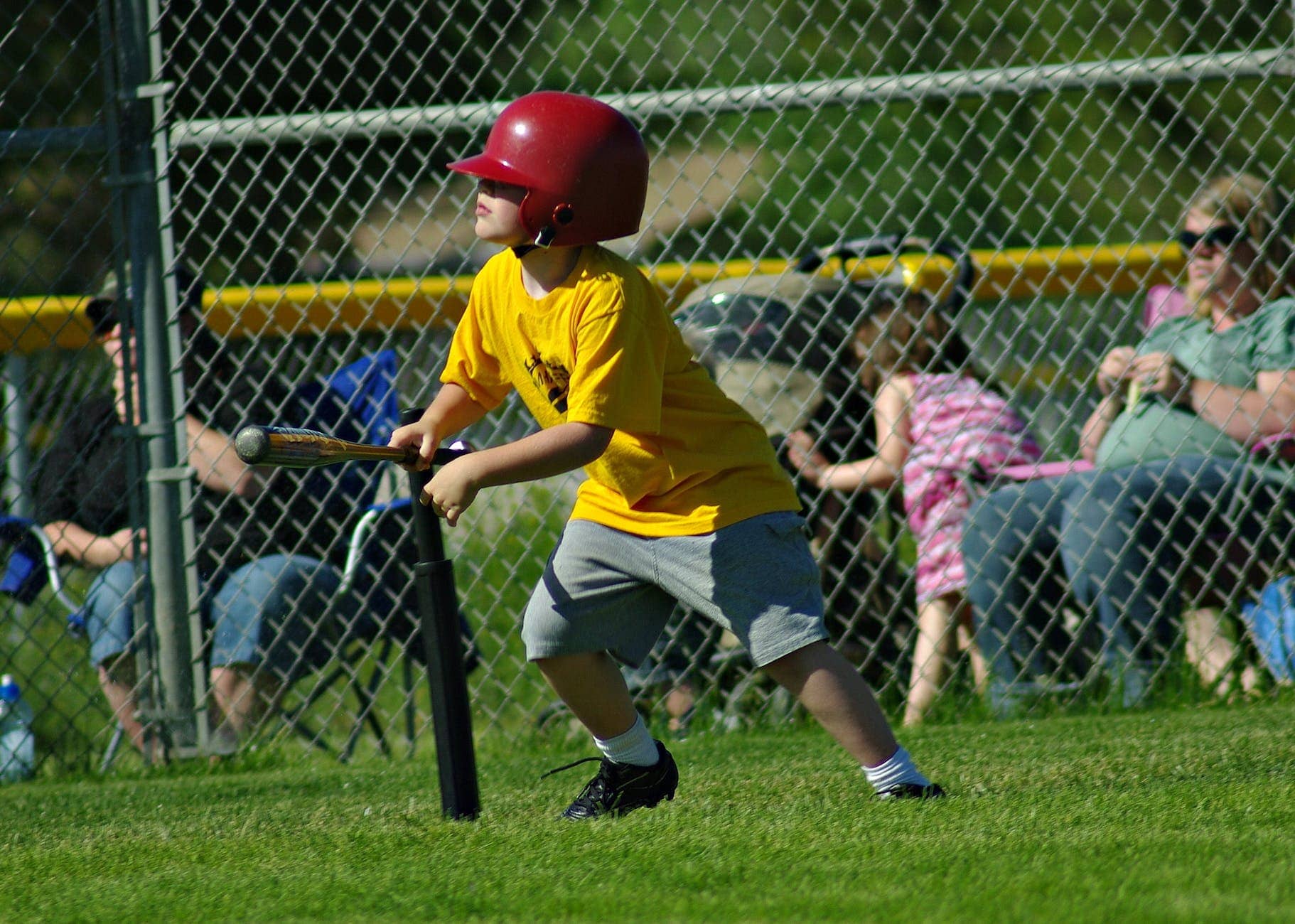 a young boy in yellow shirt wearing a red batting helmet while playing baseball